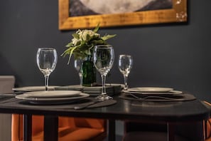 Une table à manger dressée avec des assiettes, des verres et des couverts, agrémentée d’un vase de fleurs et d’un tableau encadré accroché au mur derrière.
