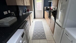 A compact kitchen with a washing machine, a refrigerator, and a coffee maker. - Apartment Sleeps 4 With Enclosed Garden (Birmingham)
