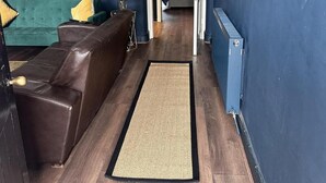 A hallway with a brown leather sofa, a woven rug, and a blue wall. - Apartment Sleeps 4 With Enclosed Garden (Birmingham)