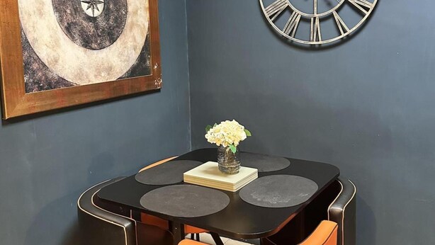 A dining table with a vase of flowers, a clock, and a framed artwork on the wall. - Apartment Sleeps 4 With Enclosed Garden (Birmingham)