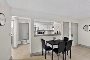 Eine moderne Küche mit weißen Schränken, einem Edelstahlkühlschrank und einem Essbereich mit schwarzem Tisch und Stühlen.