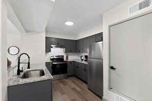 A modern kitchen with grey cabinets, stainless steel appliances, and a granite countertop. - Modern 1-bedroom apartment in Lenexa (Lenexa)