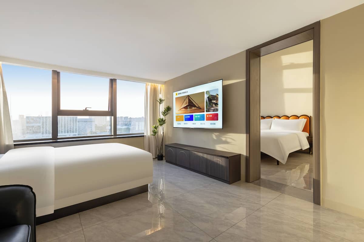 A modern hotel room with a large bed, a TV mounted on the wall, and a city view through the window.