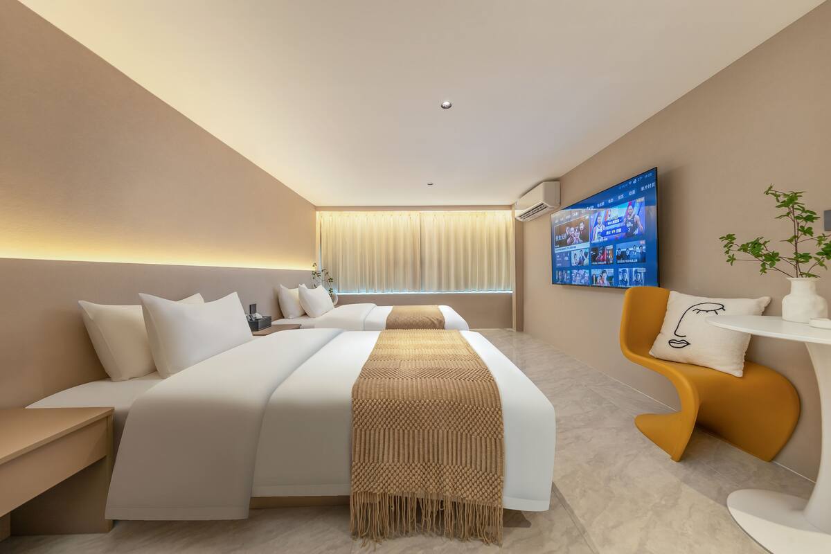 A modern hotel room with a large bed, a TV mounted on the wall, a small table, and a unique orange chair.