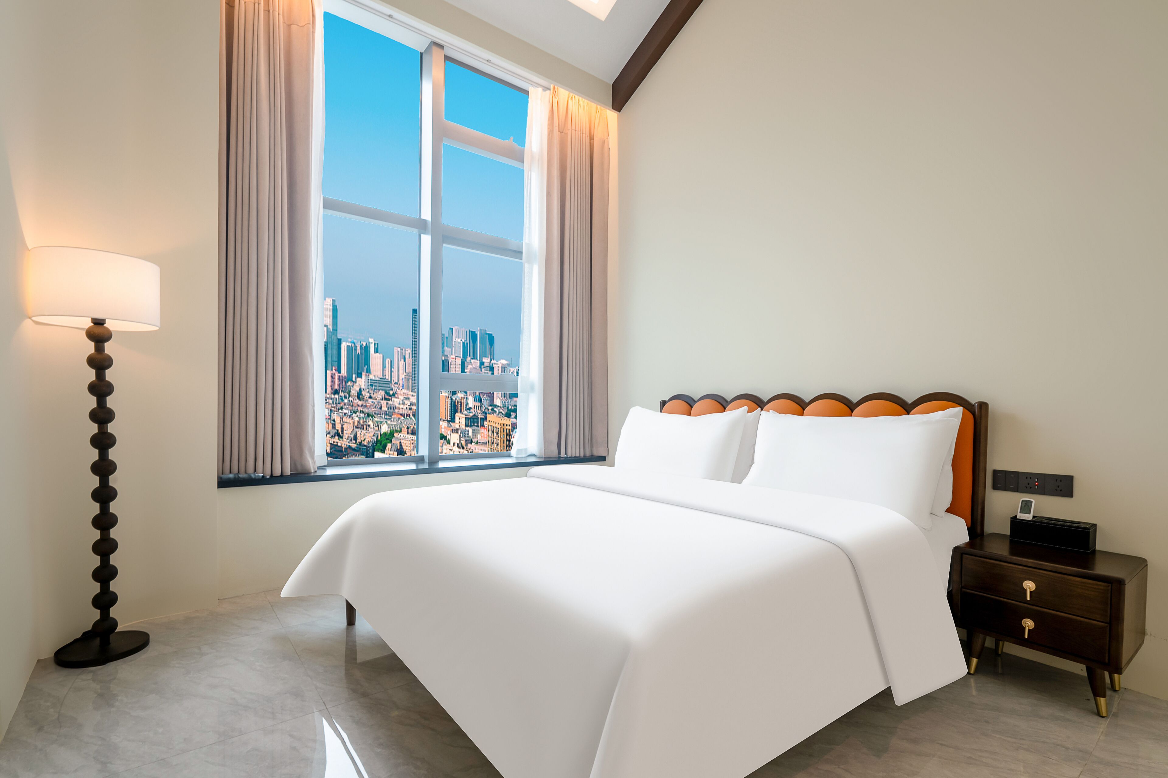 Une chambre d’hôtel avec un grand lit, une table de chevet, une lampe et une vue sur le paysage urbain par la fenêtre.