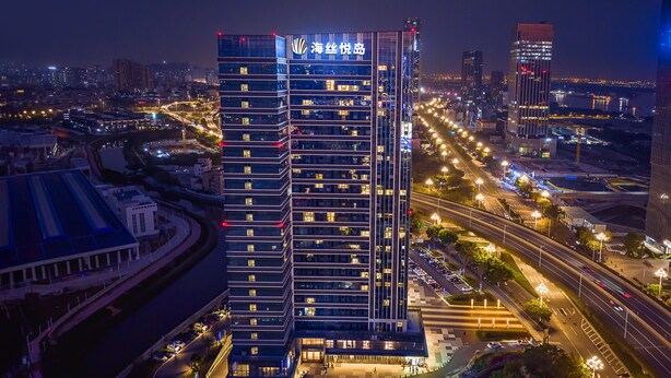 A high-rise hotel with multiple floors, a prominent entrance, and a surrounding urban environment with roads and other buildings.