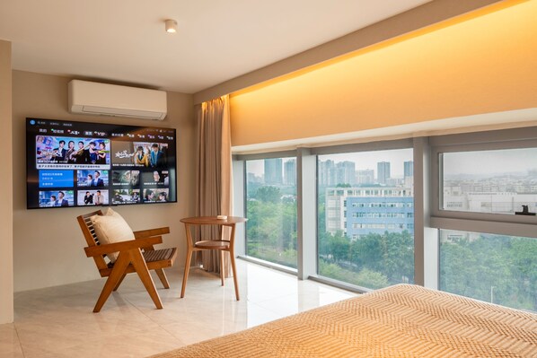 Una habitación de hotel moderna con un televisor grande en la pared, un sofá, una mesita y un ventanal con vistas a la ciudad.