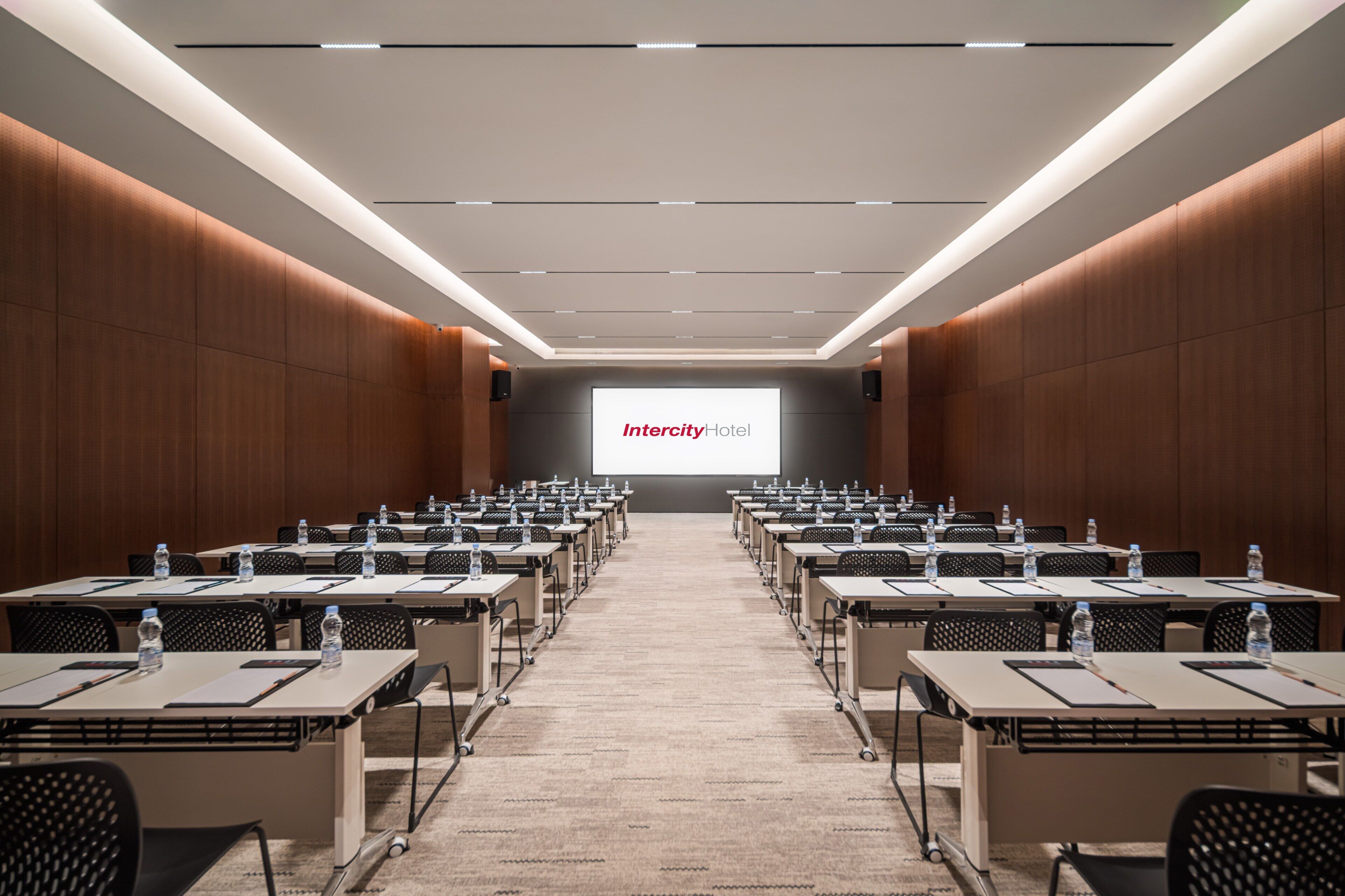 A conference room with rows of tables, chairs, and a large screen displaying 'Intercity Hotel'.