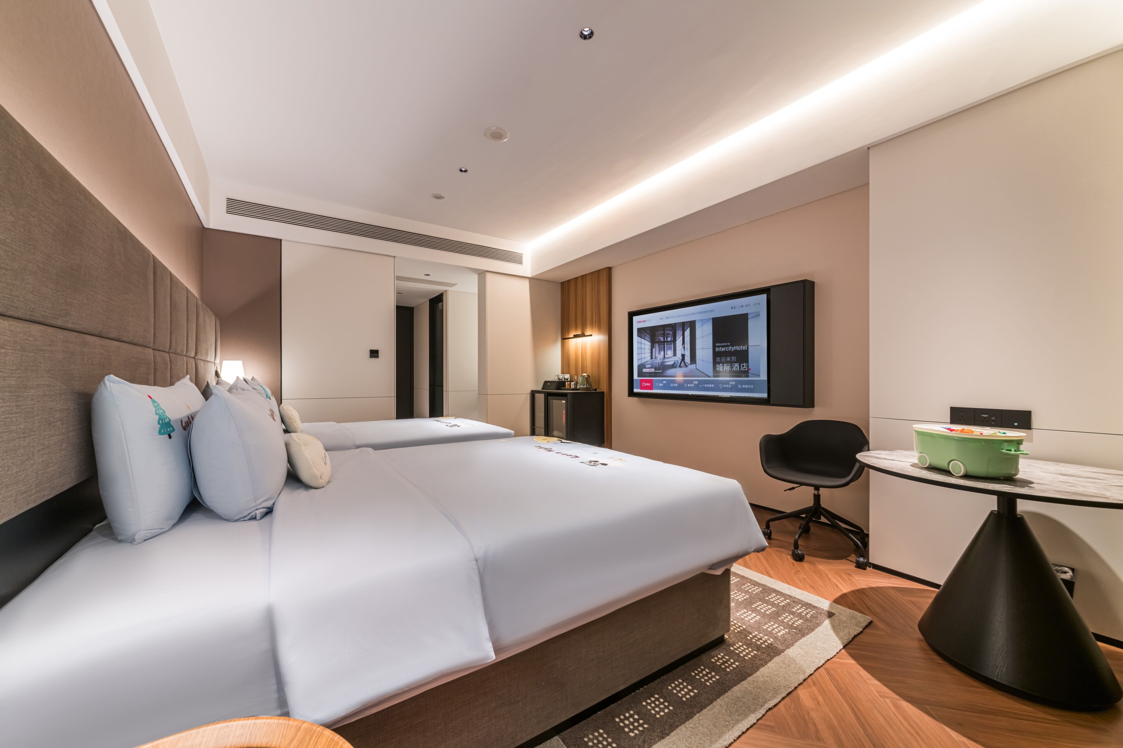 Une chambre d’hôtel avec un lit, un bureau, une chaise, une télévision et une petite table sur laquelle se trouve un récipient vert.