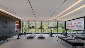 Un gimnasio con cintas de correr, bicicletas estáticas y una pantalla grande que muestra 'Intercity Hotel'.