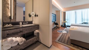 Habitación de hotel moderna con tocador de mármol, cama grande, vistas a la ciudad y un baño bien iluminado.