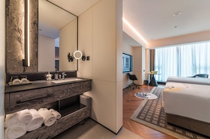 Habitación de hotel moderna con tocador de mármol, cama grande, vistas a la ciudad y un baño bien iluminado.