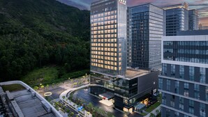Un edificio moderno con fachada de vidrio, rodeado de vegetación y un paisaje montañoso.