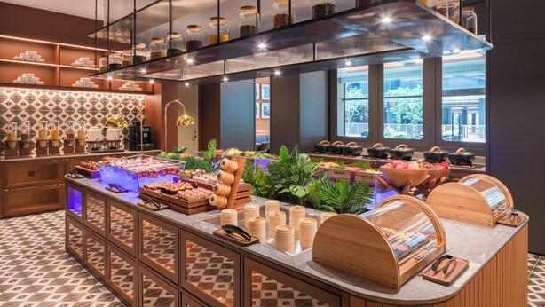 Un amplio buffet de desayuno moderno con diversas opciones de comida, un ventanal con vista a la ciudad y un suelo con estampado.