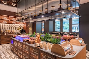 Un amplio buffet de desayuno moderno con diversas opciones de comida, un ventanal con vista a la ciudad y un suelo con estampado.