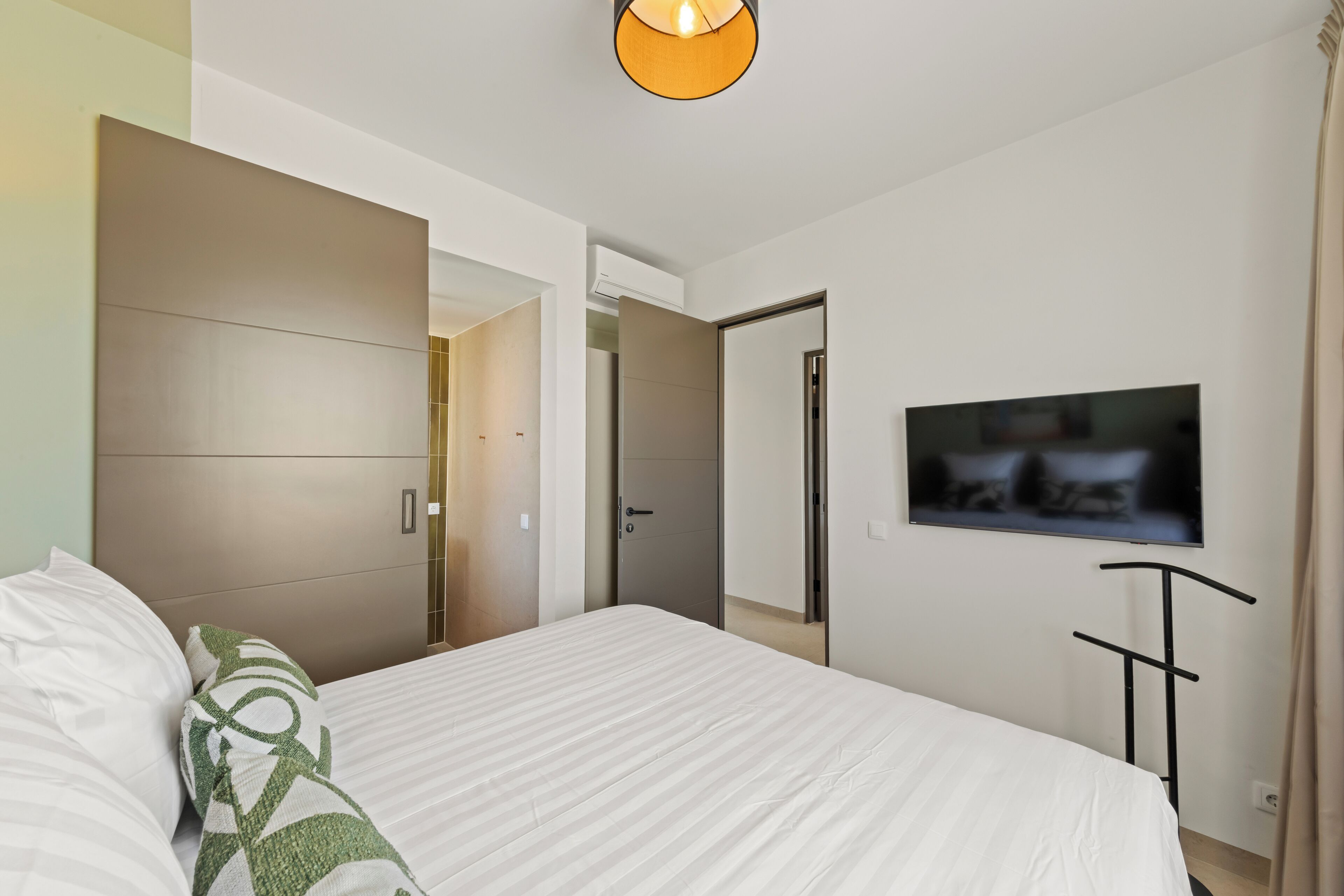 A modern hotel room with a large bed, a flat-screen TV, and a wardrobe.