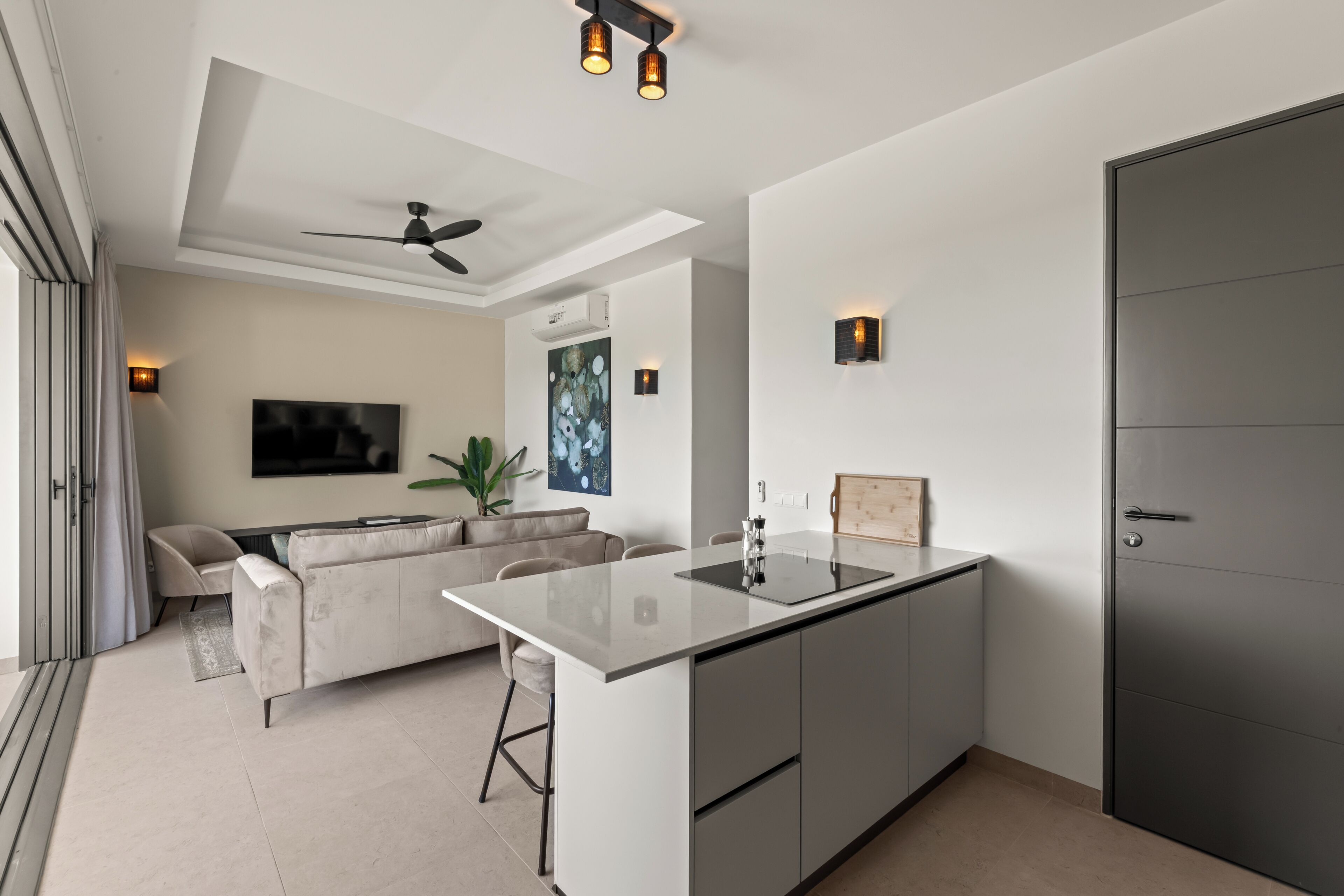 Uma cozinha moderna com ilha central, ventilador de teto, iluminação embutida e uma porta grande.