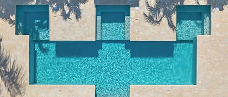 A rectangular pool with clear water, surrounded by stone walls and palm tree shadows.