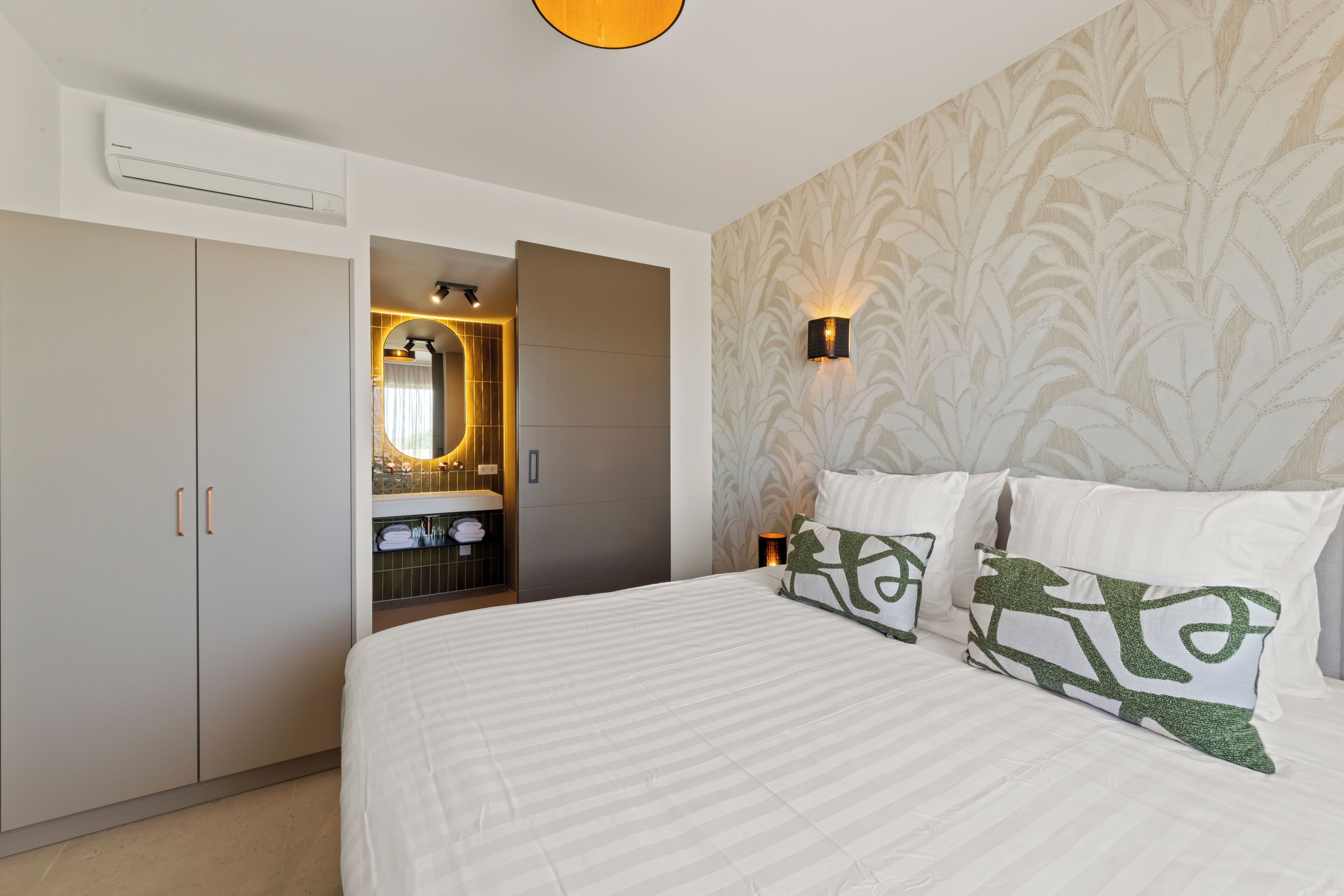 Un dormitorio con cama, armario, espejo y lámpara de pared.