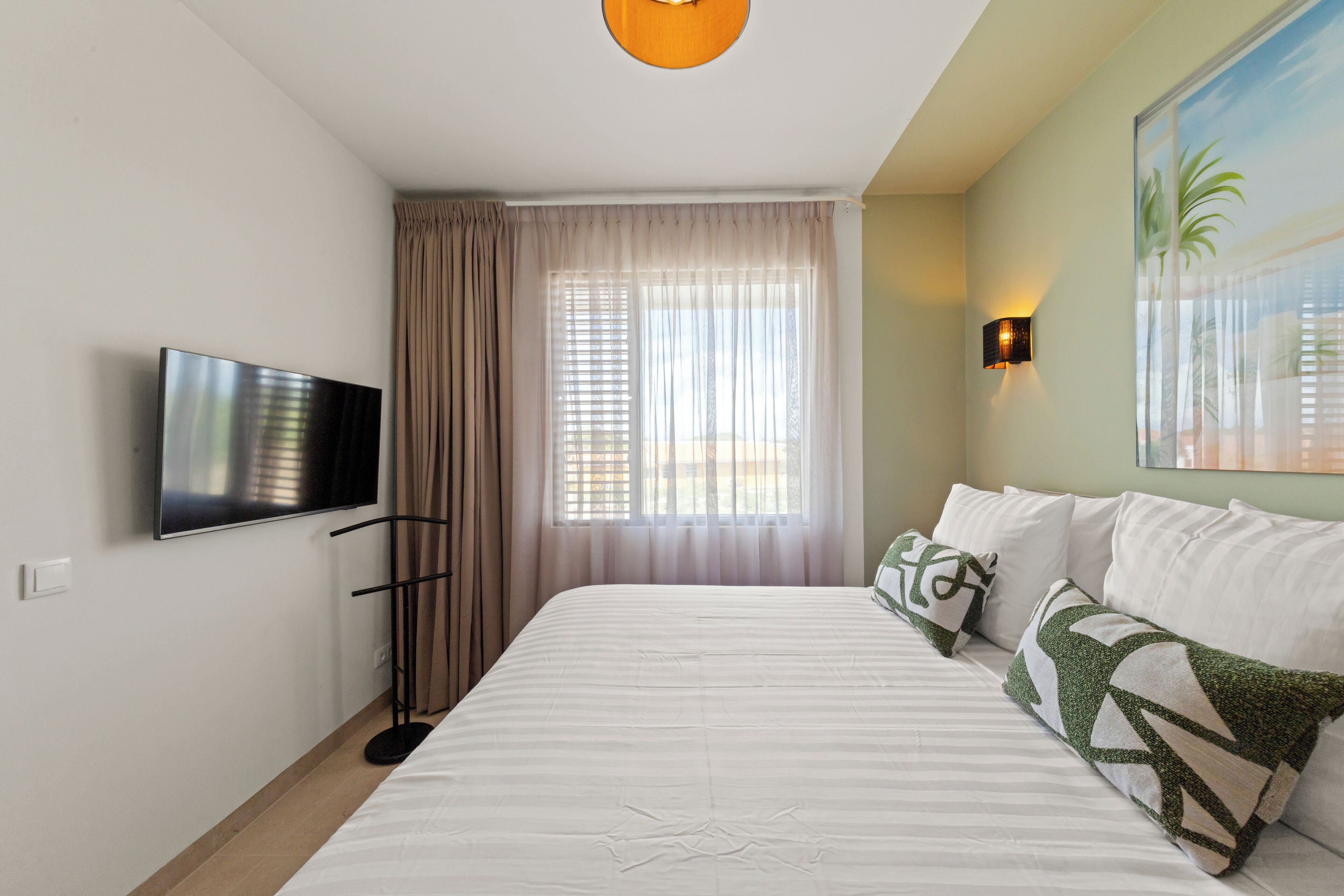 Een hotelkamer met een bed, gordijnen, een televisie, een wandlamp en een schilderij.