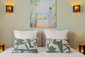 Un dormitorio con cama, dos almohadas, un cuadro y dos apliques de pared.