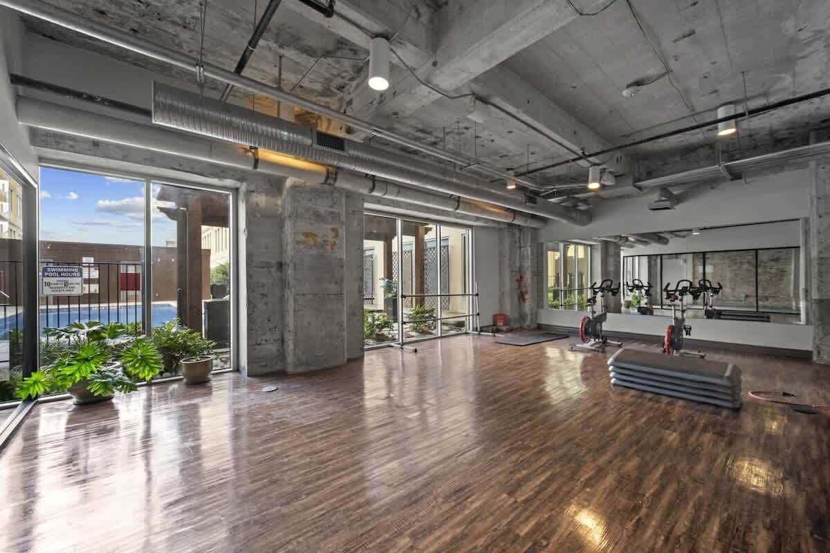 Un interior con pilares de concreto, amplias ventanas y equipo de ejercicio.