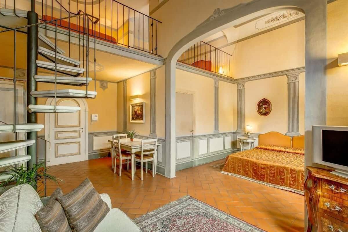 Amplia sala de estar con techo alto, una escalera, zona de comedor y un dormitorio con televisor.