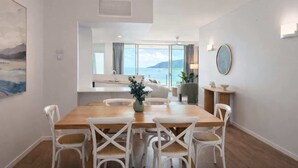 Ein Essbereich mit Holztisch und weißen Stühlen, Meerblick durch große Fenster und ein modernes Interieur.