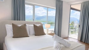 Ein Hotelzimmer mit einem großen Bett, Blick auf Berge und ein Gewässer, sowie ein Balkon mit Vorhängen.