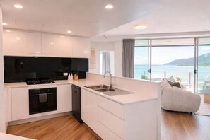 A modern kitchen with a built-in oven, a dishwasher, and a large island with a sink. - Luxury 3BR Coral Coast Home w/ Oceanfront (Cairns City)