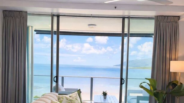 Ein modernes Wohnzimmer mit einer Couch, einem runden Couchtisch und Blick auf den Ozean durch große Glasfenster.