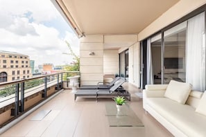 Ein Balkon mit einer Couch, zwei Loungestühlen, einem Blumentopf und einem Tisch.