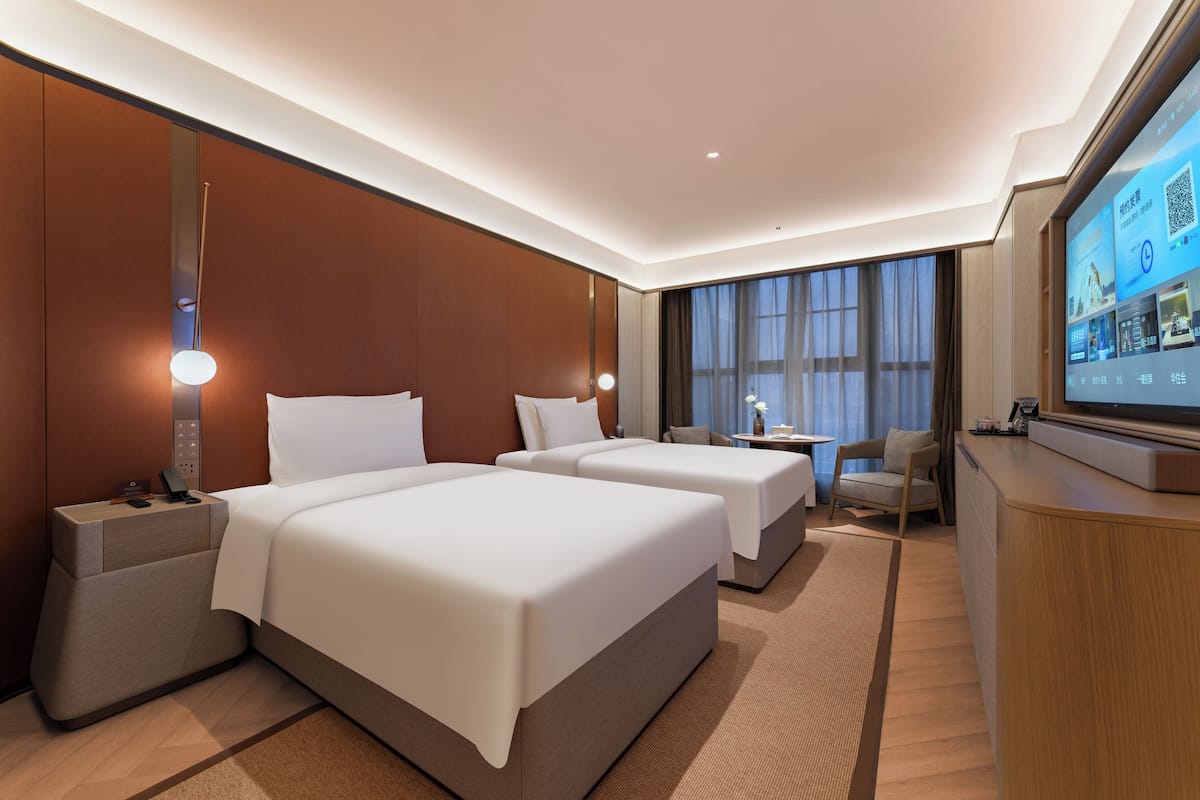 A hotel room with two beds, a TV, a desk, and a chair.