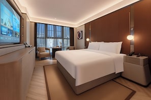 Quarto de hotel moderno com uma cama grande, uma escrivaninha com computador, uma mesa pequena e uma cadeira.
