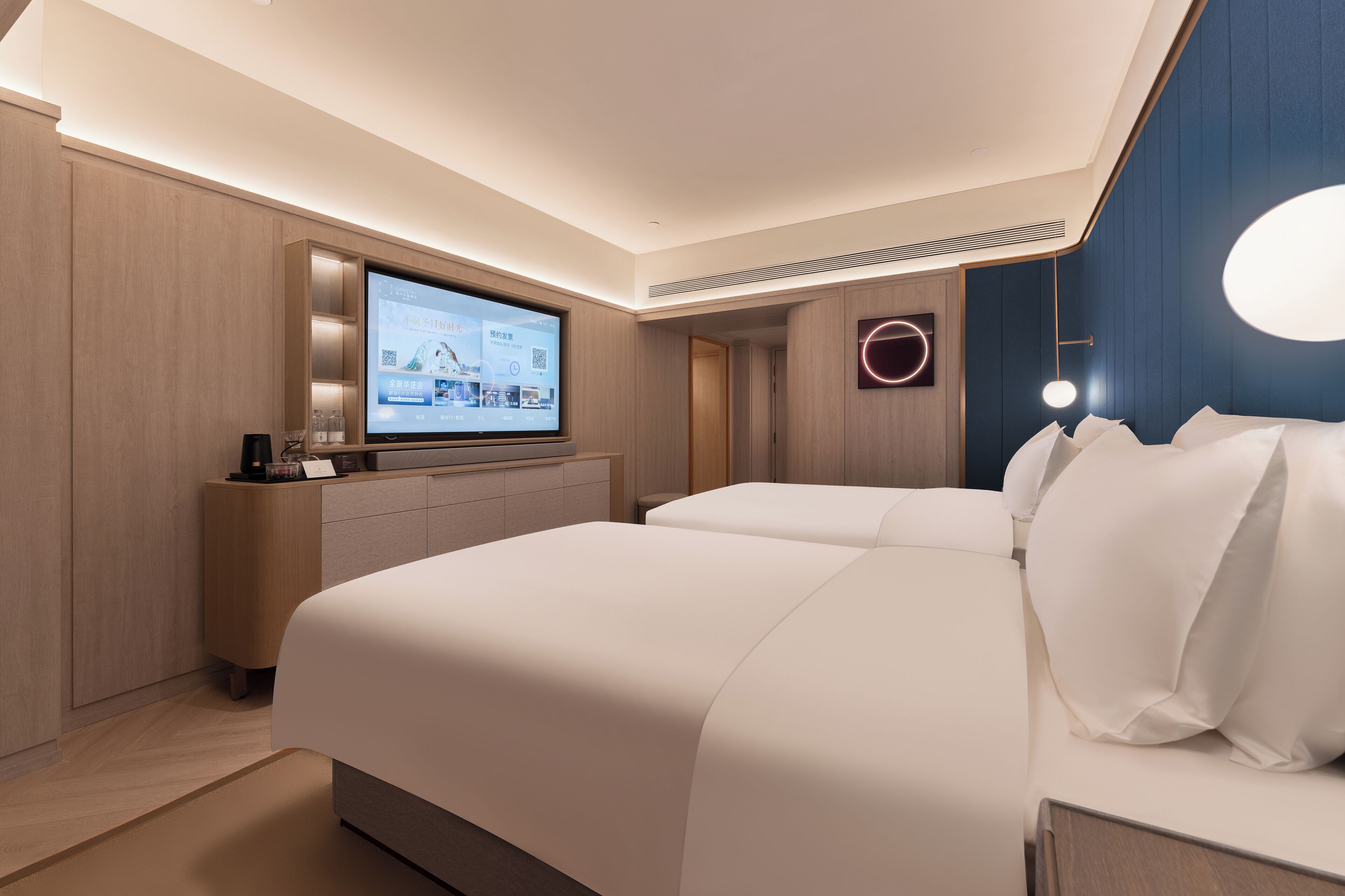 A modern hotel room with a large bed, a flat-screen TV, a bedside table, and a wall-mounted light fixture.