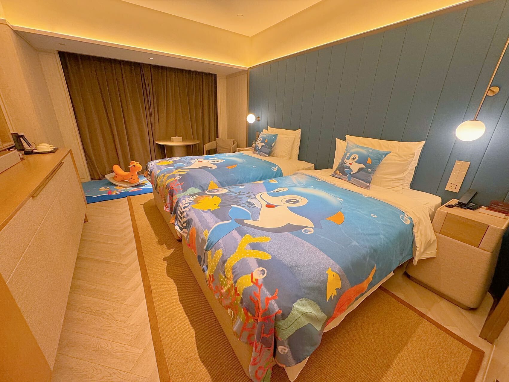 Een hotelkamer met twee bedden, een bureau, een stoel, een klein tafeltje en een gordijn.