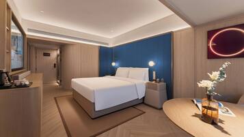 A modern hotel room with a bed, bedside tables, a desk, and a wall-mounted artwork.
