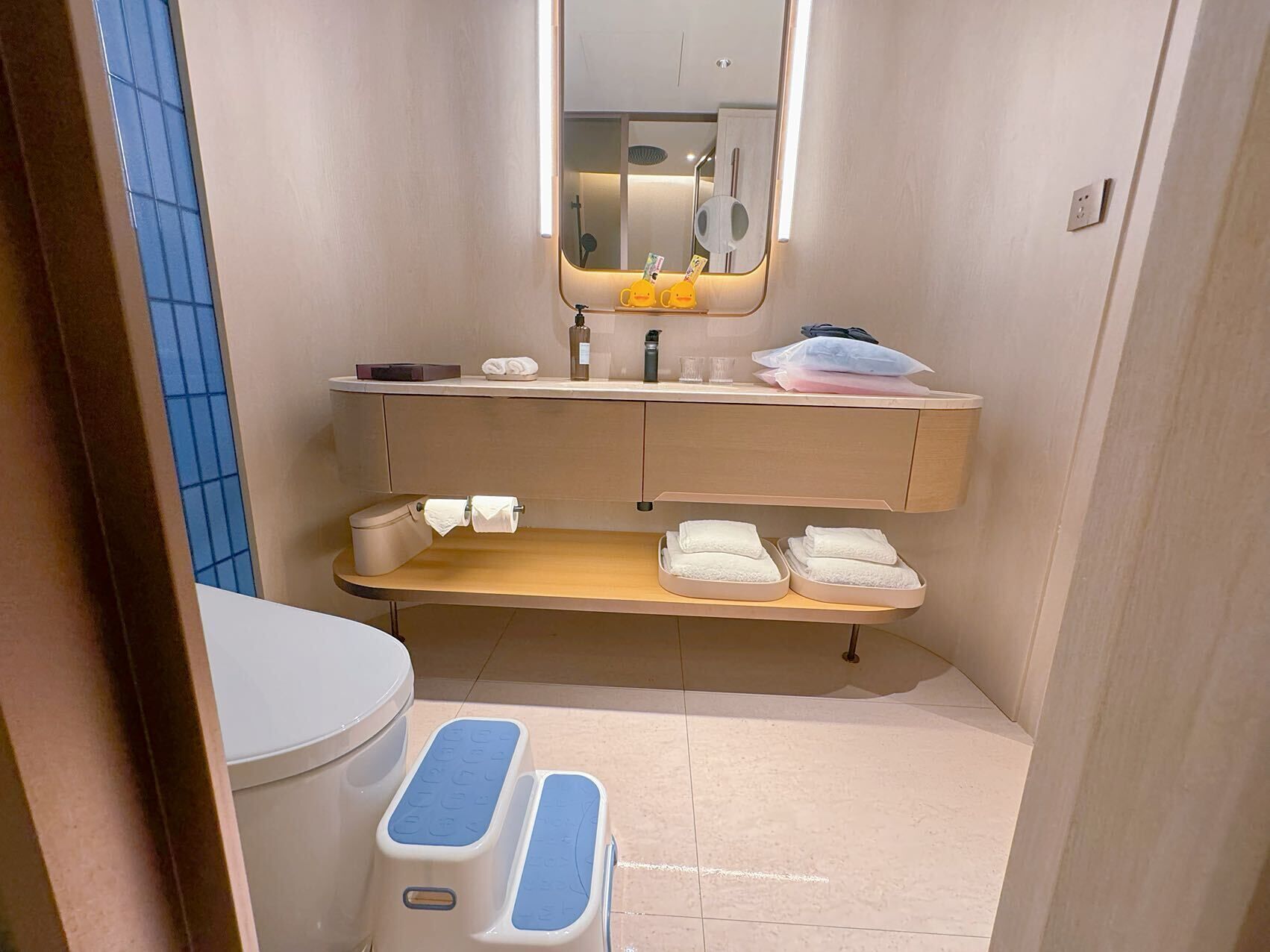 A compact bathroom with a toilet, a sink, a mirror, and a shelf with towels.