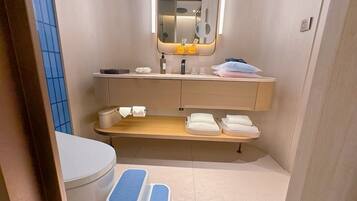 A compact bathroom with a toilet, a sink, a mirror, and a shelf with towels.