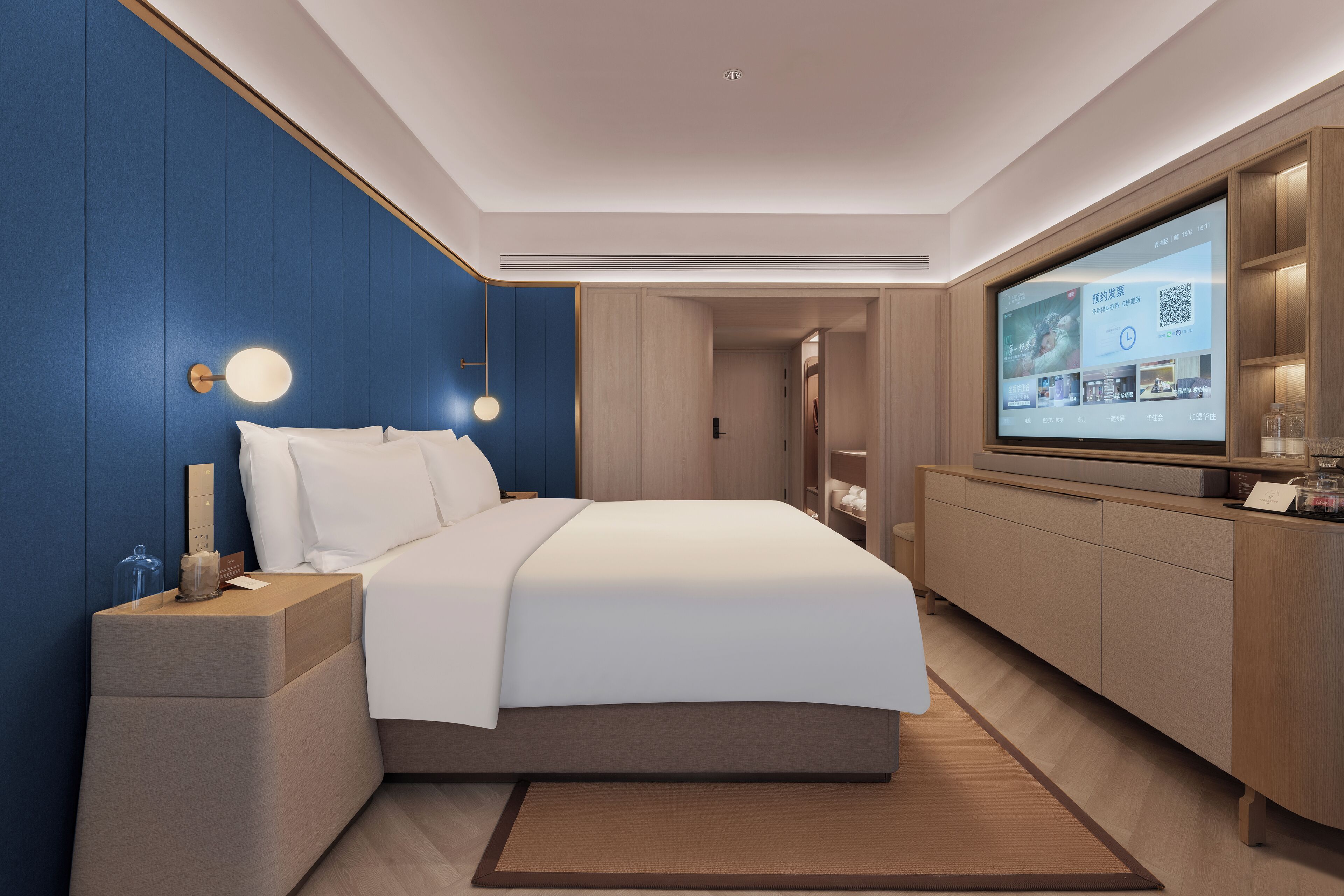 Una habitación de hotel moderna con una cama grande, un televisor montado en la pared y un armario de madera.
