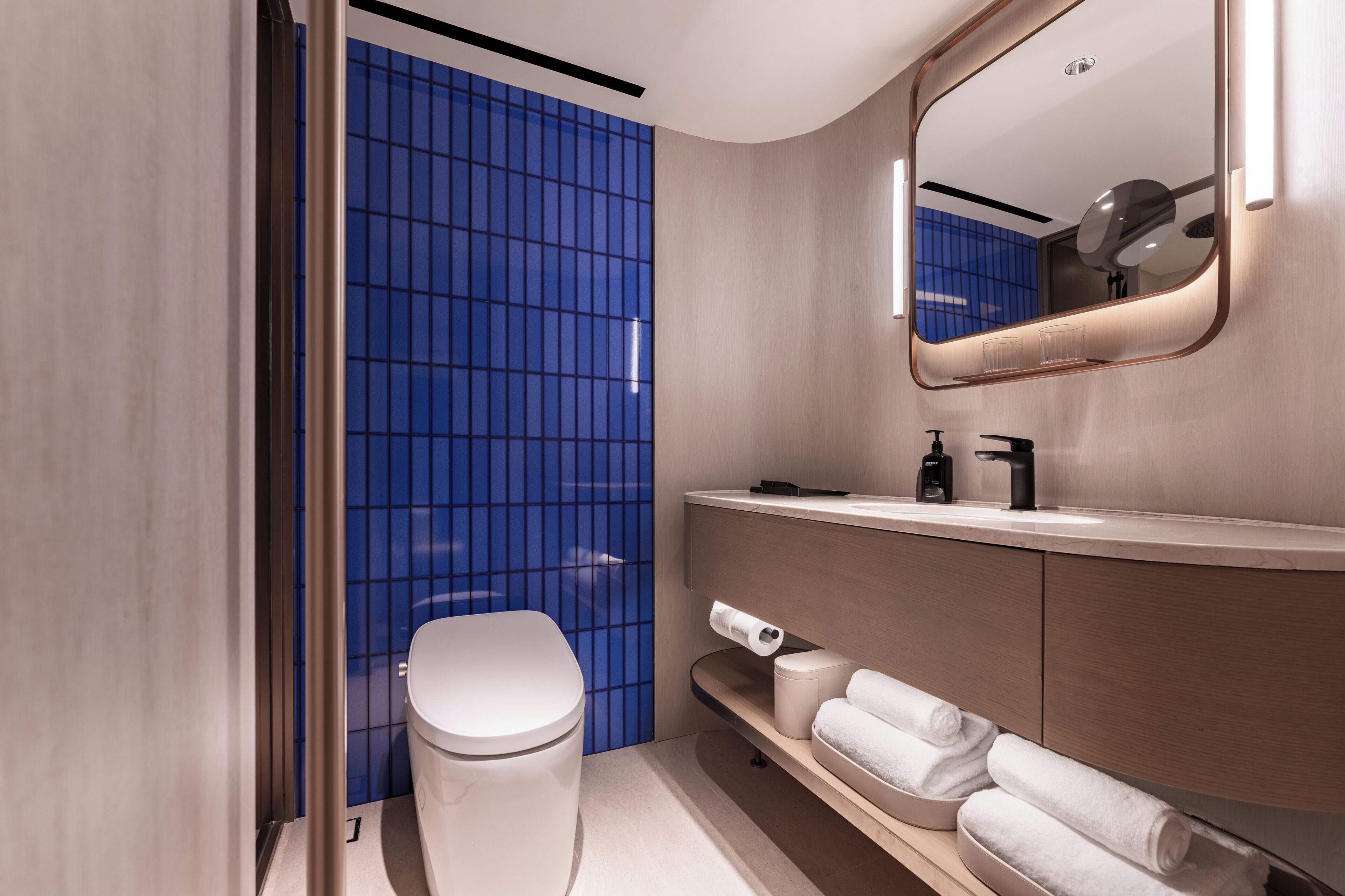 Ein modernes Badezimmer mit Toilette, Waschbecken mit Spiegel und Ablagefläche für Handtücher.