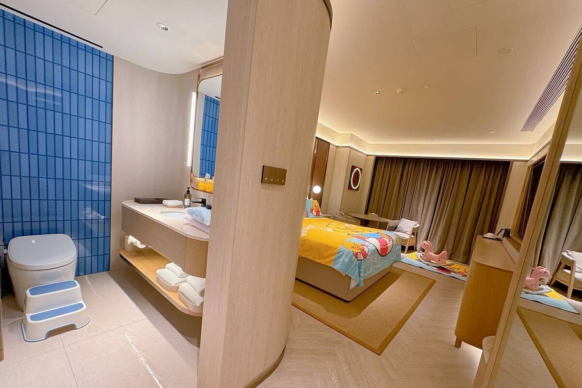 A modern hotel room with a large bed, a bathroom with a sink and toilet, and a mirror.