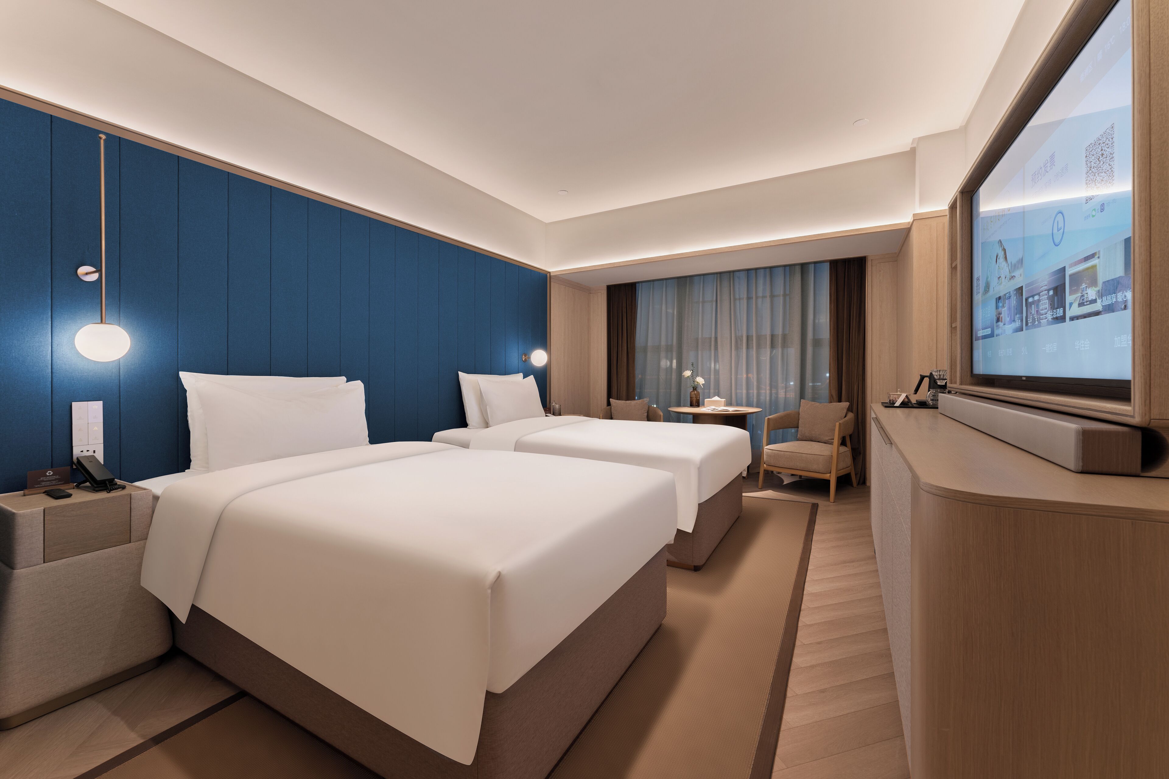 Une chambre d’hôtel avec deux lits, un bureau, une chaise, une télévision et une grande fenêtre.