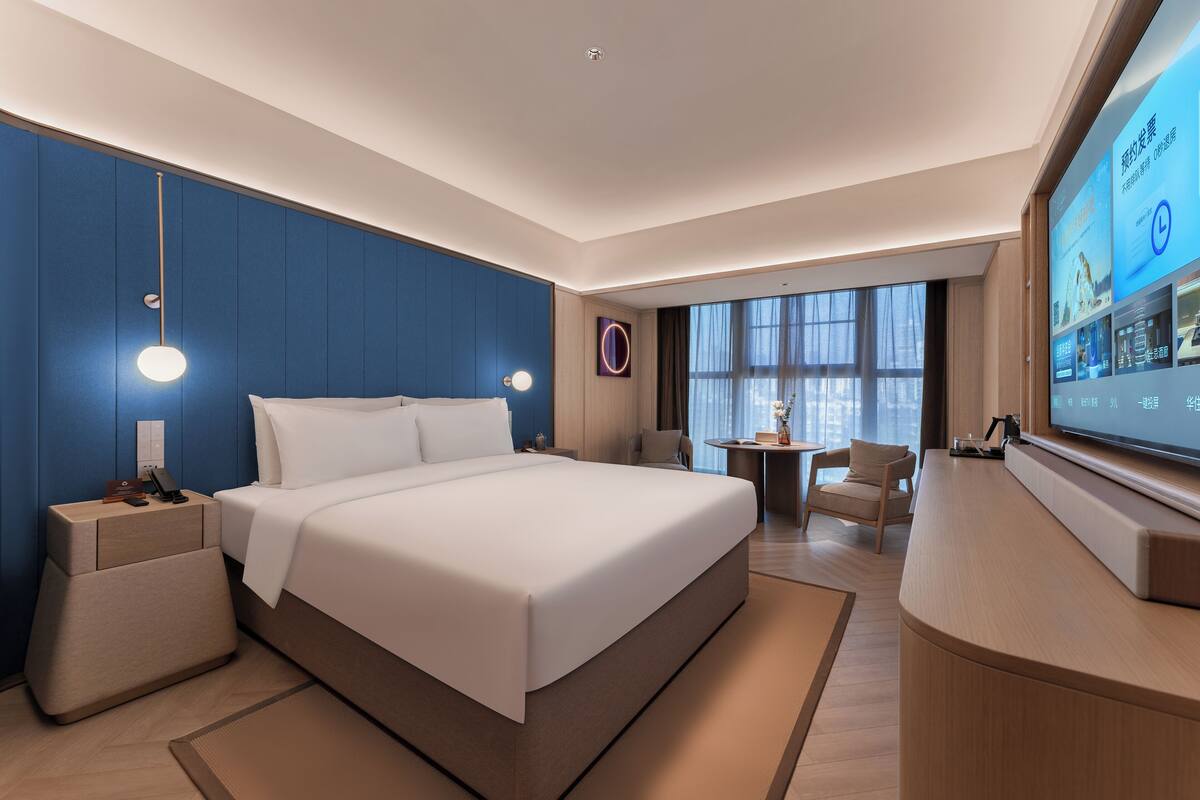 A modern hotel room with a large bed, bedside tables, a desk, and a TV.