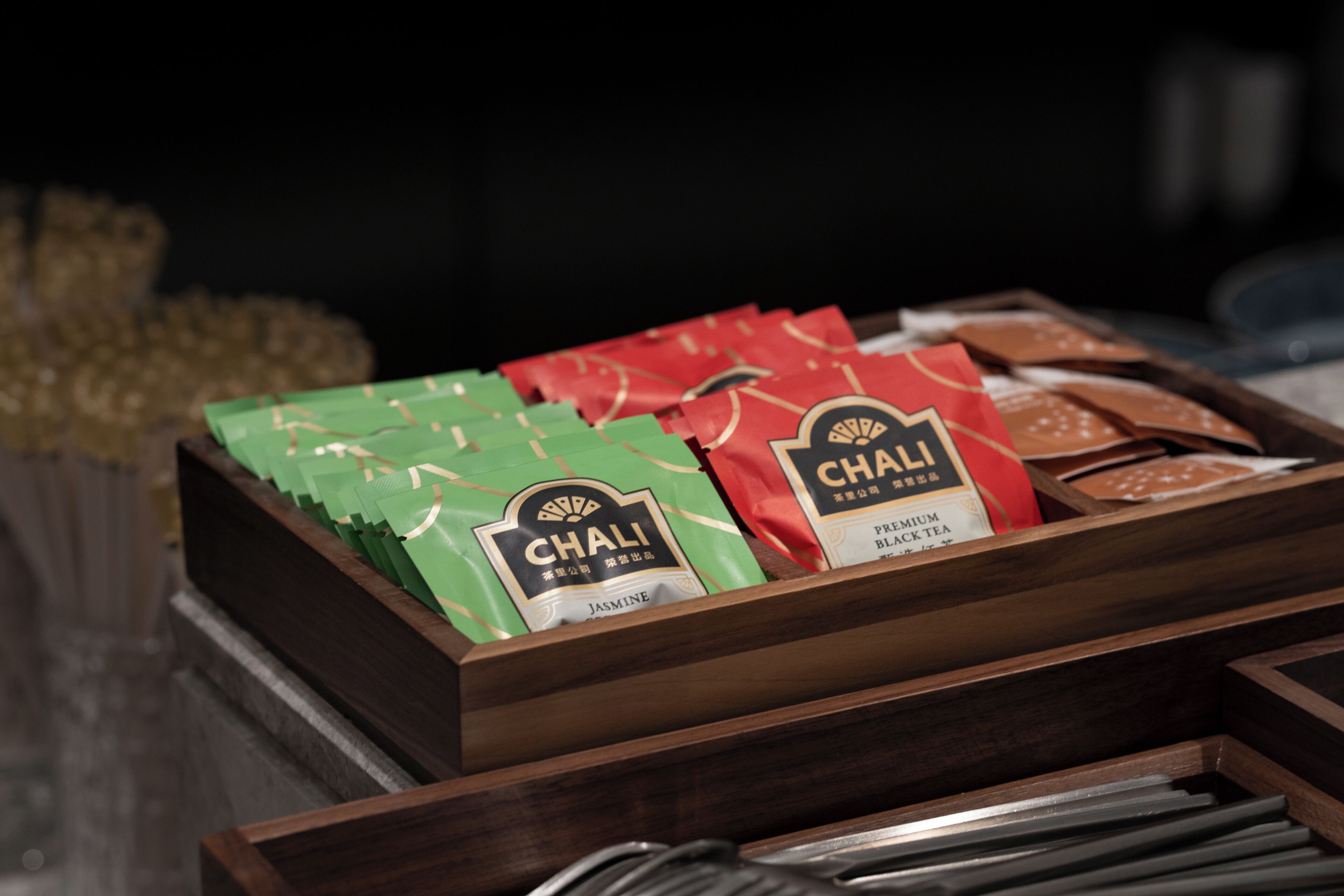 A wooden box containing various tea packages labeled 'Chali' with different flavors like 'Jasmine' and 'Premium Black Tea.'