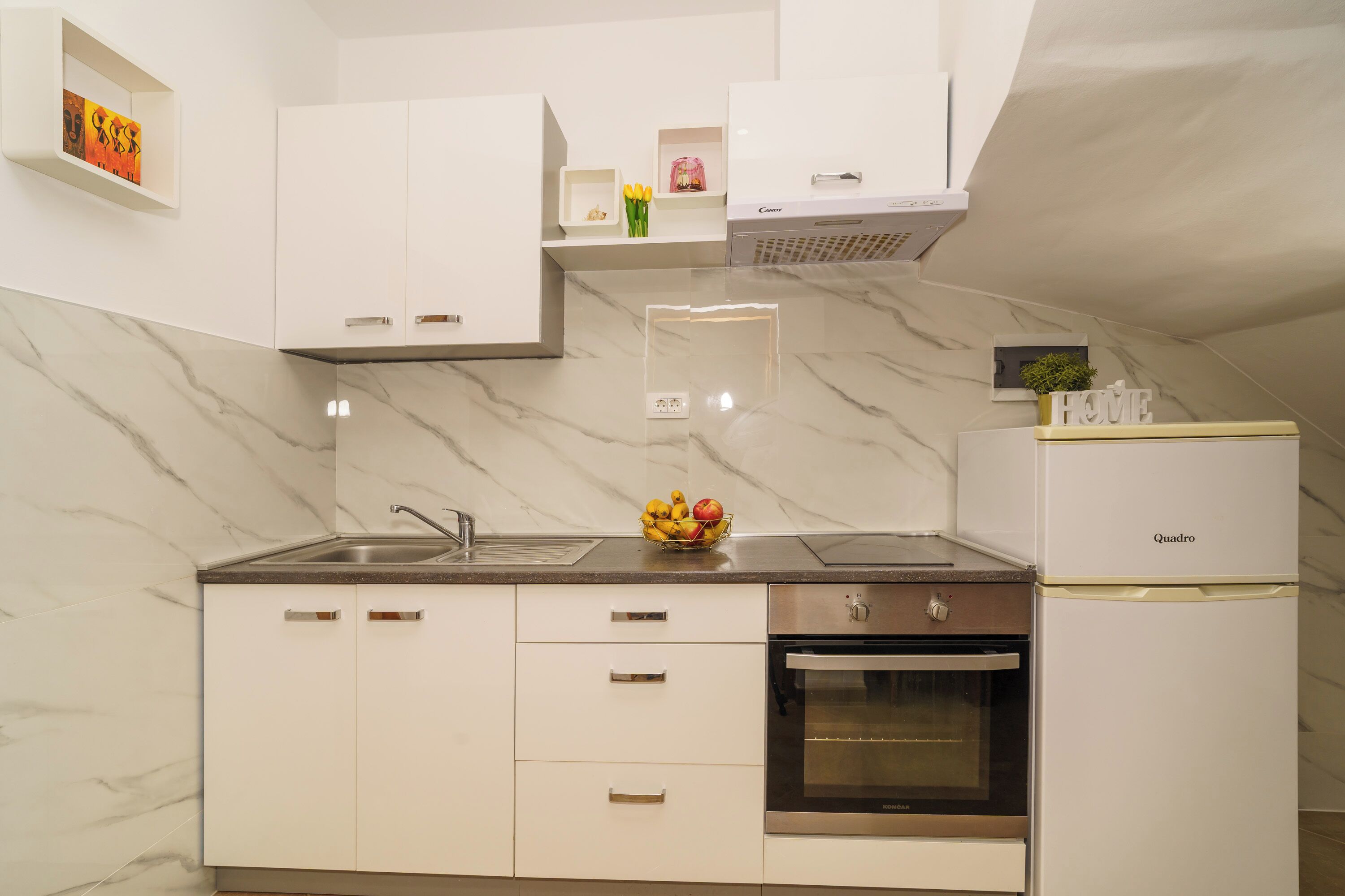 A modern kitchen with white cabinets, a marble backsplash, a built-in oven, and a refrigerator.