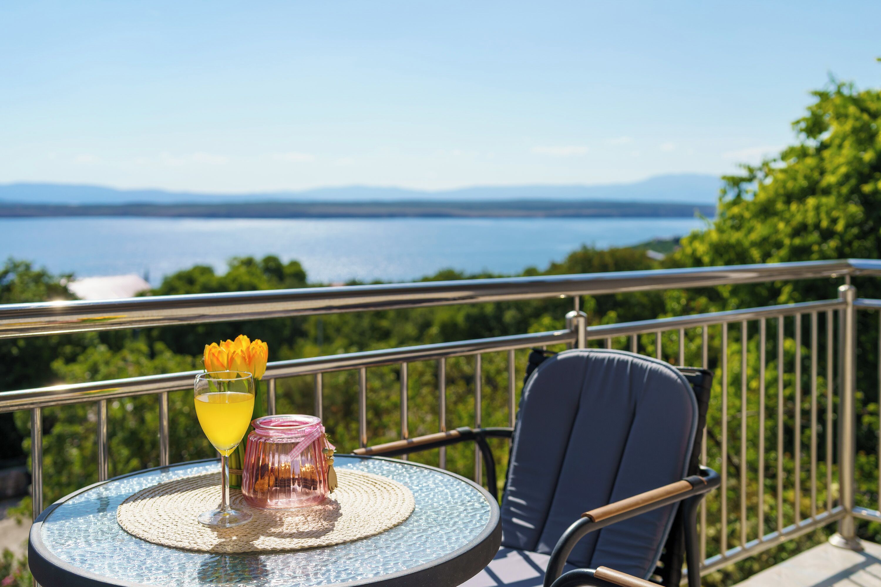 Un balcon avec une table, une chaise, un verre et une fleur.