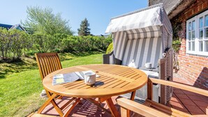 A wooden table and chairs outside a building with a brick wall and a thatched roof. - Friesenhaus Käpt'n Hahn, house part 04 (Westerland)
