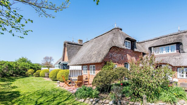 A house with a thatched roof, a brick exterior, and a well-maintained garden with a lawn and hedges. - Friesenhaus Käpt'n Hahn, house part 04 (Westerland)