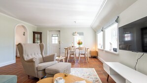 A living room with a sofa, ottoman, coffee table, and a TV. There is a dining area with a table and chairs. - Friesenhaus Käpt'n Hahn, house part 04 (Westerland)